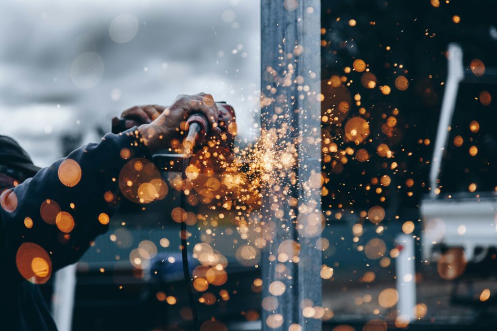 Industrial worker operating metal fabrication equipment with sparks flying in a manufacturing environment, representing engineering excellence, industrial operations and production leadership. Livingston James provides industrial executive search services to manufacturing, engineering, supply chain and industrial organisations across Scotland and the UK.